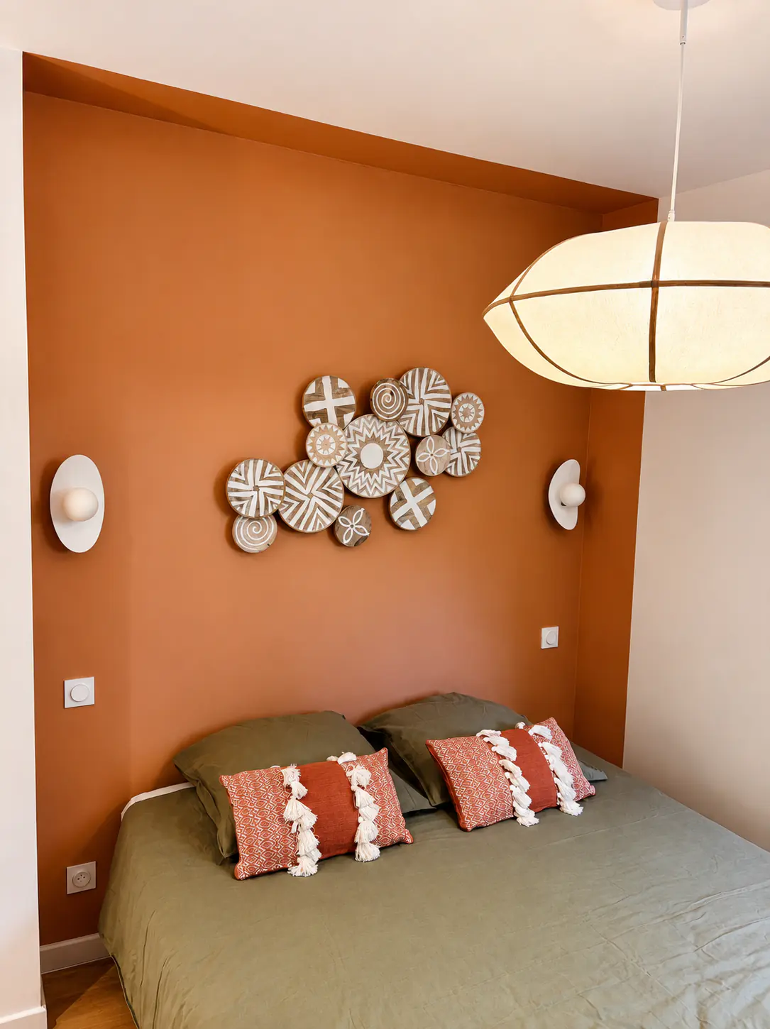 Chambre paisible aux murs terracotta, décoration murale balinaise en bois et linge de lit vert sauge