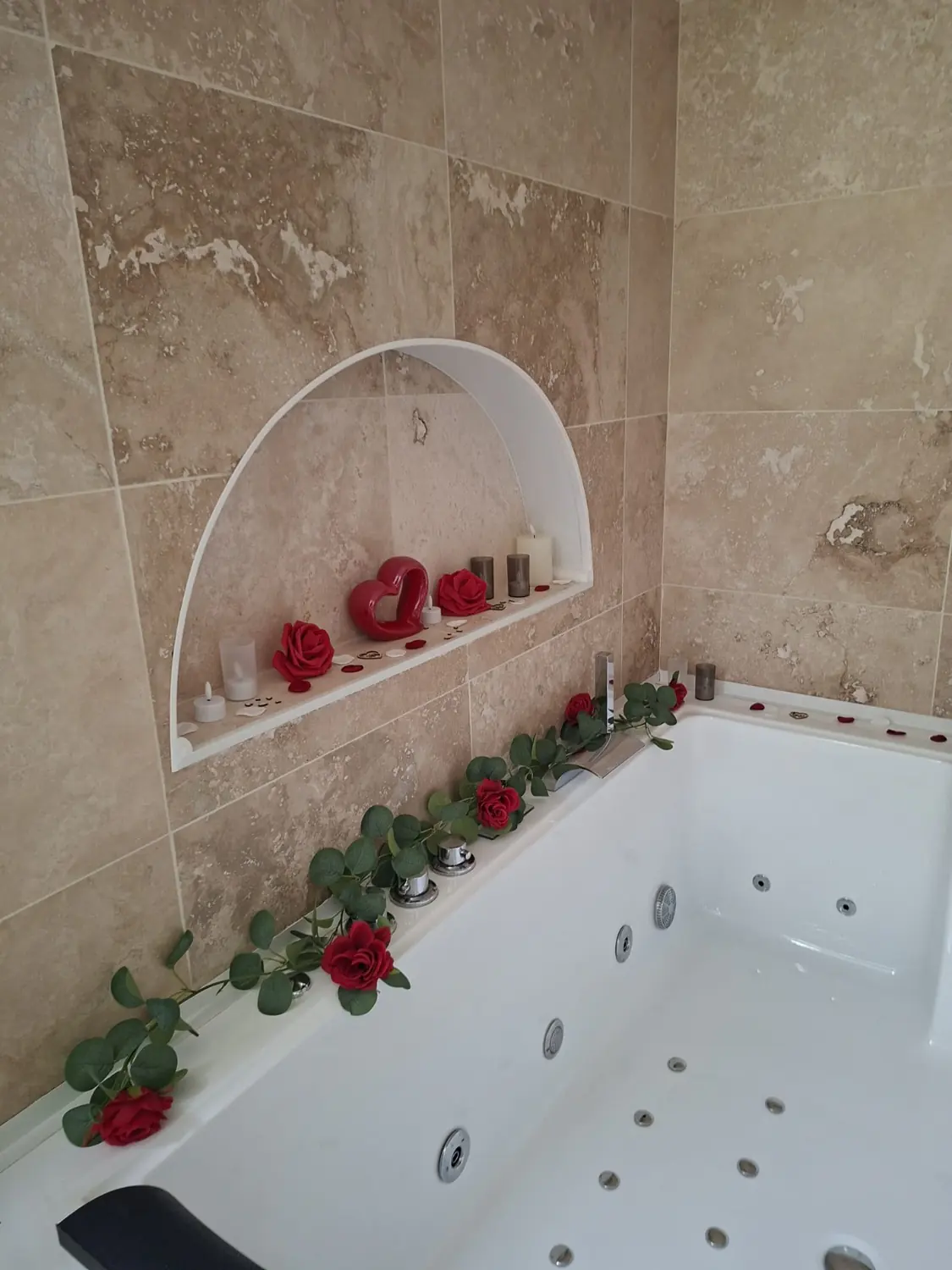 Baignoire balnéo privative habillée de travertin, niche avec bougies et roses